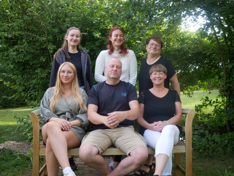 Team der Einrichtung im Garten auf einer Bank sitzend